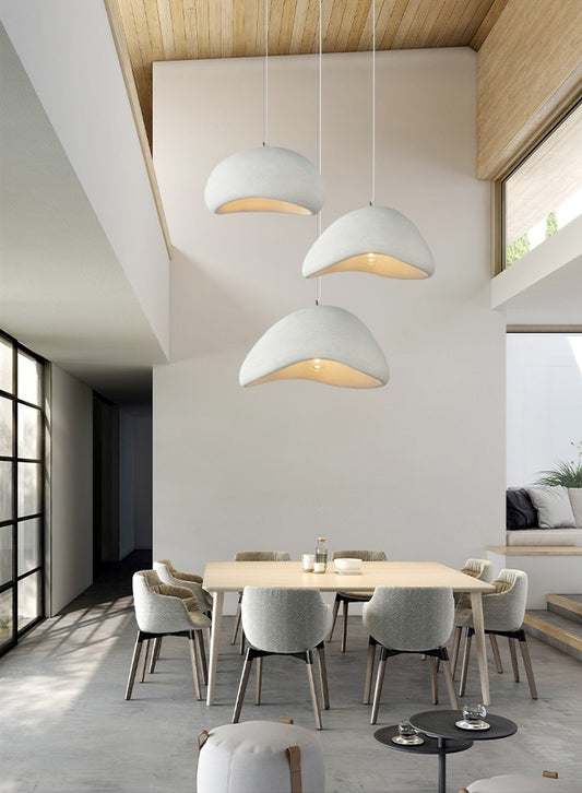 salle à manger moderne et lumineuse avec haut plafond sur lequel sont accrochés trois grandes suspensions luminaires design